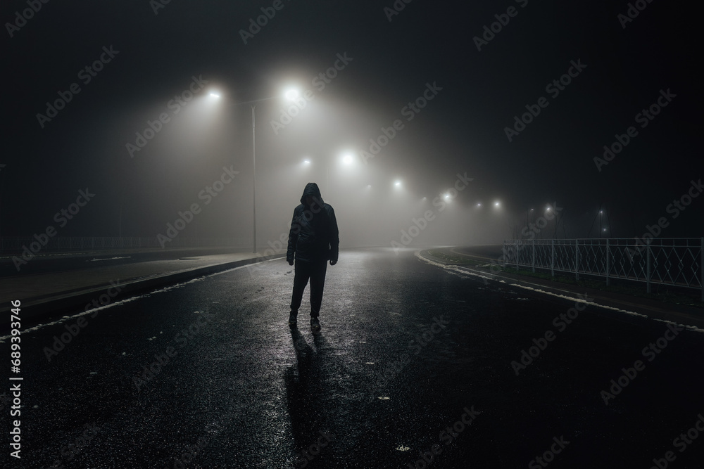 Sad man alone walking along the alley in night foggy road - obrazy, fototapety, plakaty 