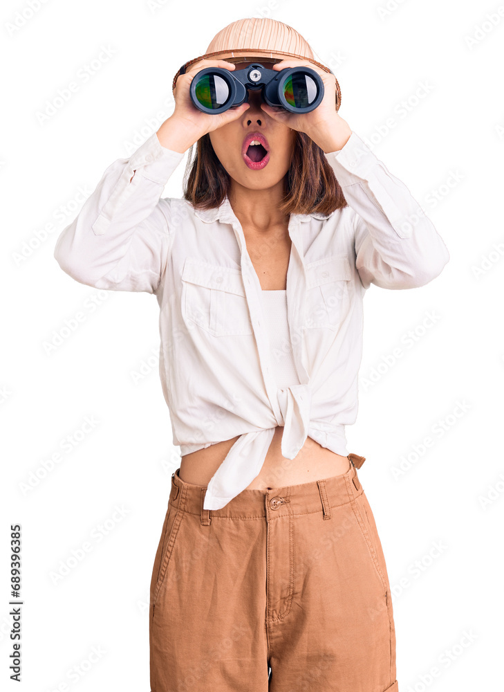 Young beautiful chinese girl wearing explorer hat holding binoculars scared and amazed with open mouth for surprise, disbelief face