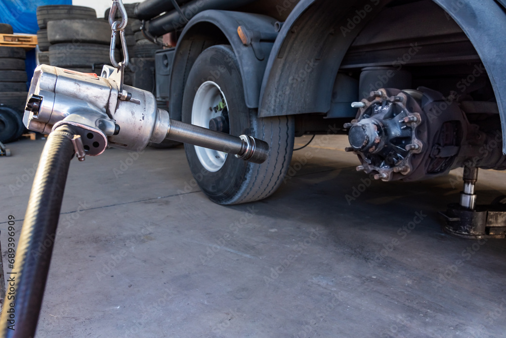 Fototapeta premium Compressed air tool to remove wheel bolts in a tire shop, with a truck with a wheel removed.