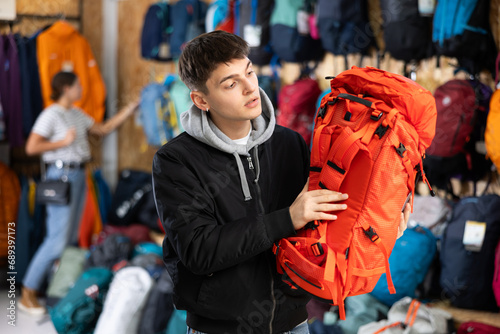 Young guy tourist chooses tourist backpack for winter hike in a tourist equipment store