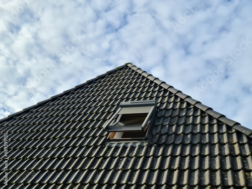 Open roof window in velux style with black roof tiles.