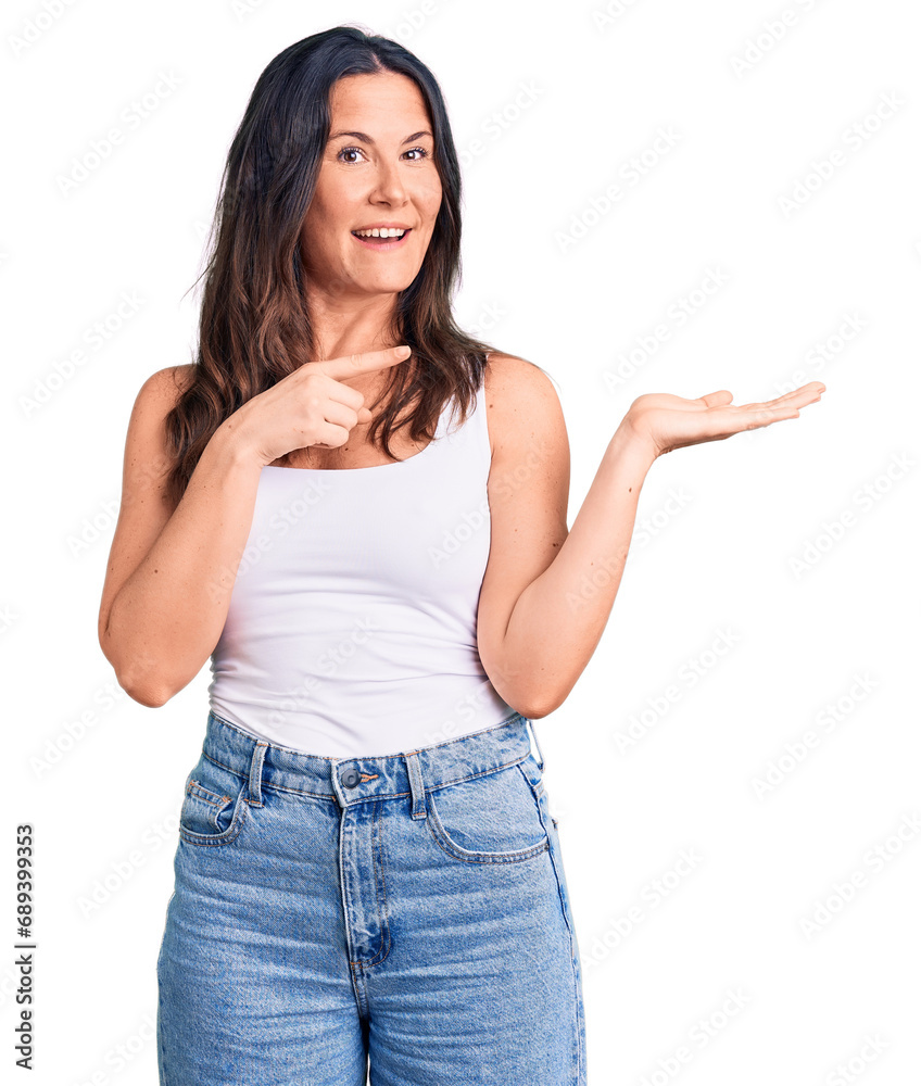 Young beautiful brunette woman wearing casual sleeveless t-shirt amazed and smiling to the camera while presenting with hand and pointing with finger.