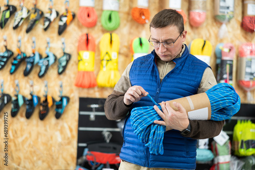 Male tourist chooses and buys climbing rope for an winter hike in a tourist equipment store