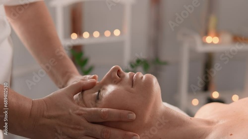 A woman relaxes on a massage table, feeling how tension moves away from stress, and muscles gain harmony. The hands of the masseur massage the head of the client beauty salon. Harmony and relaxation photo