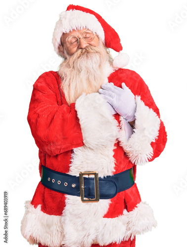 Old senior man with grey hair and long beard wearing traditional santa claus costume smiling with hands on chest with closed eyes and grateful gesture on face. health concept.