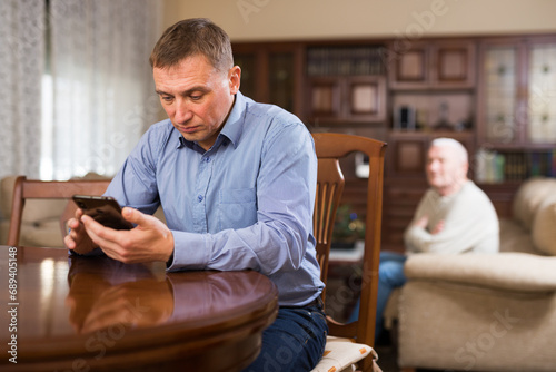 Adult son and elderly father are offended at each other because of the misunderstanding in his home photo