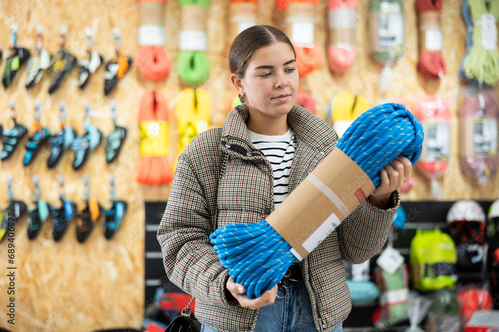 Obraz premium Young girl in winter clothes carefully selects climbing rope for winter hike in a sports equipment store