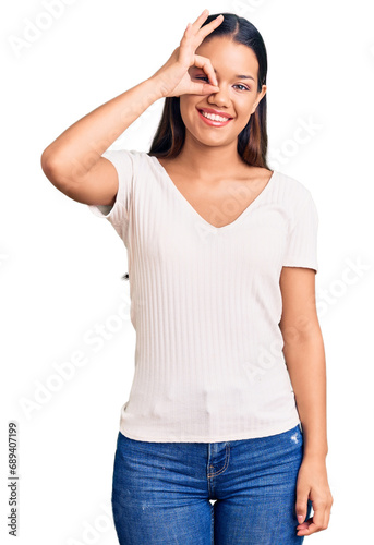 Young beautiful latin girl wearing casual white t shirt smiling happy doing ok sign with hand on eye looking through fingers