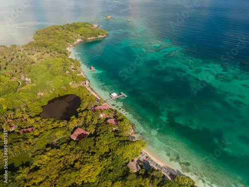 Aerial drone view from above of the tropical Caribbean island with lush green palm trees forests and sandy beaches surrounded with crystal clear turquoise shallow ocean water.