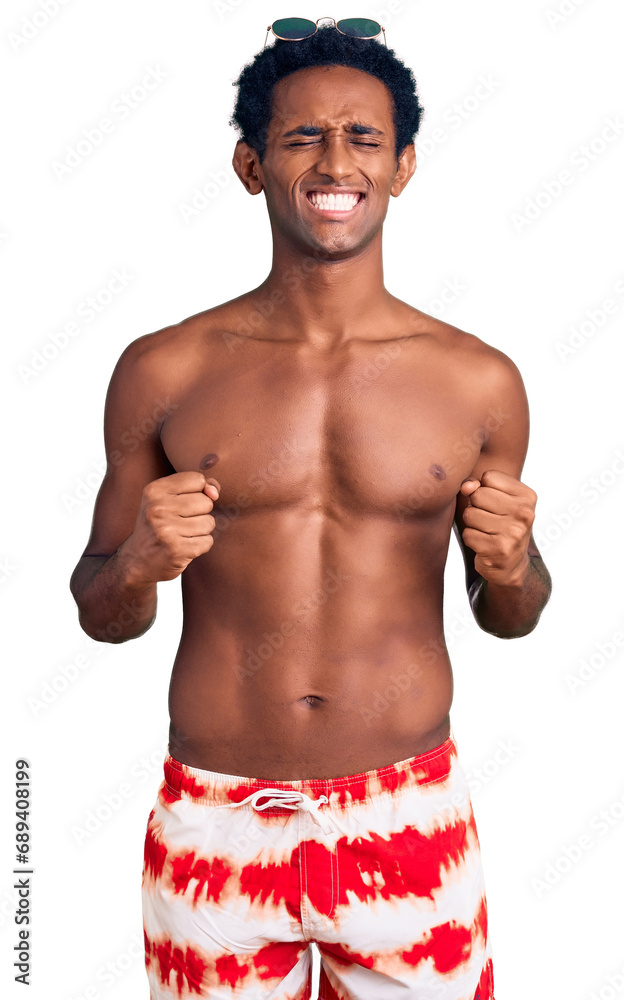 Fototapeta premium African handsome man wearing swimsuit and sunglasses excited for success with arms raised and eyes closed celebrating victory smiling. winner concept.