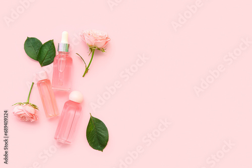 Bottles of cosmetic oil with rose extract and flowers on pink background