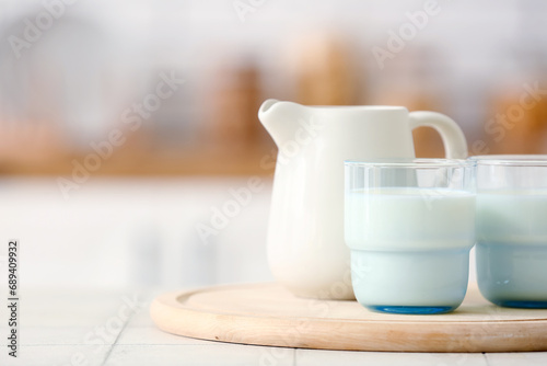 Fototapeta Naklejka Na Ścianę i Meble -  Wooden board with ceramic jug and glasses of milk on white tile table