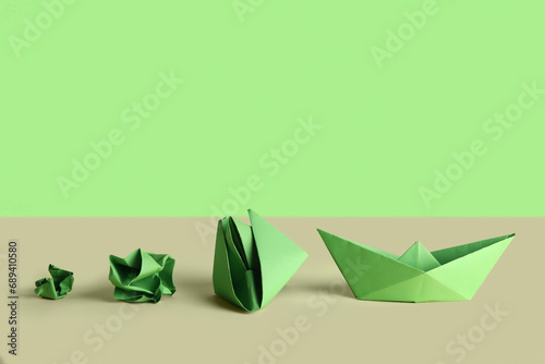 Green origami boat, flower and crumpled paper on green background