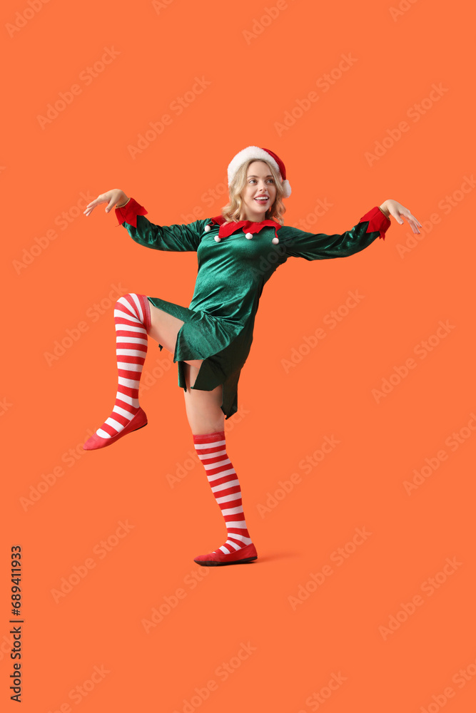 Dancing young woman dressed as elf on orange background