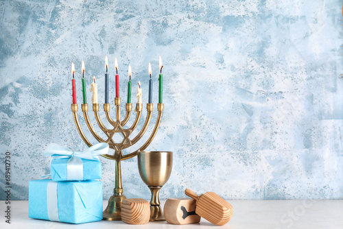 Hanukkah composition with menorah, goblet, dreidels and gift boxes on blue grunge background