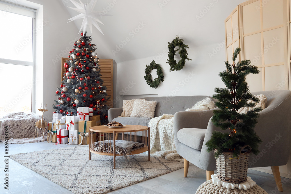 Interior of festive living room with decorated Christmas tree, gift boxes and grey sofa