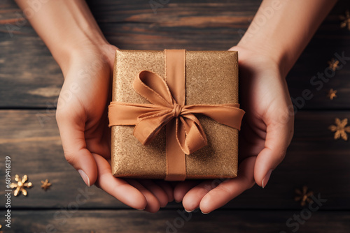 Closeup female hands holding a gift box on a wooden background. Top view. Christmas and New Year concept © mikeosphoto