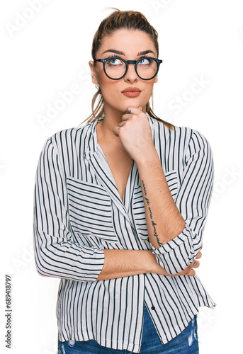 Young caucasian woman wearing business shirt and glasses with hand on chin thinking about question, pensive expression. smiling with thoughtful face. doubt concept.