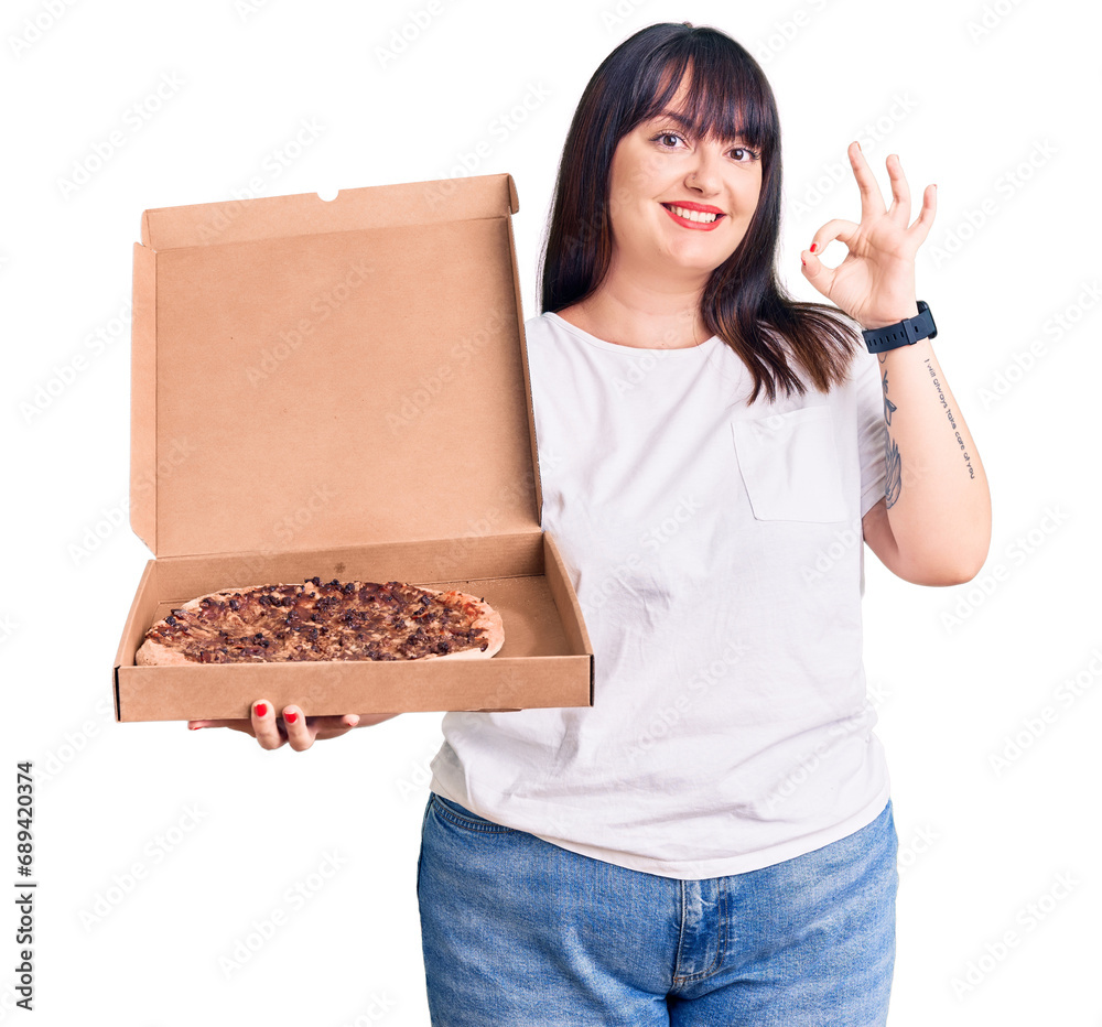 Young plus size woman holding delivery pizza box doing ok sign with fingers, smiling friendly gesturing excellent symbol Young plus size woman holding delivery pizza box doing ok sign with fingers, smiling friendly gesturing excellent symbol