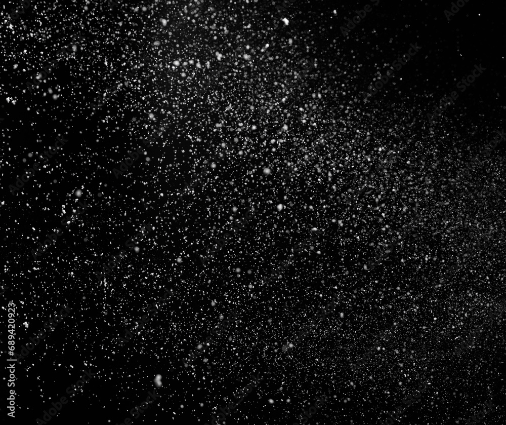 Freezing falling snowflakes or stardust in air on black background for overlay blending mode. Stopping the movement of white powder on a dark background, selective focus