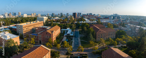 Panoramic early morning view of a serene university campus, blending historic brick buildings with modern high-rises, surrounded by lush greenery and distant ocean vistas.