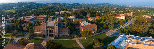 Aerial view of UCLA campus in Westwood, Los Angeles, showcasing Romanesque Revival architecture, modern buildings, green spaces, and a serene city backdrop under a partly cloudy sky.