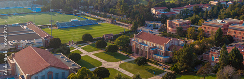 Aerial view of UCLA's campus, blending traditional and modern architecture, with a prominent stadium, greenery, and clear skies, conveying a serene academic atmosphere.