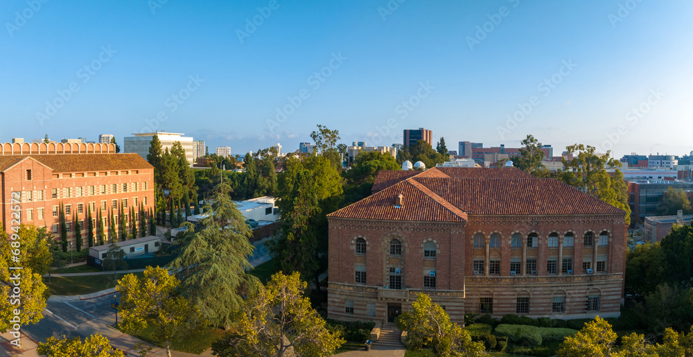 Aerial view of the University of Southern California campus, showcasing historic red-brick buildings, lush greenery, and a scenic city backdrop under a clear blue sky.