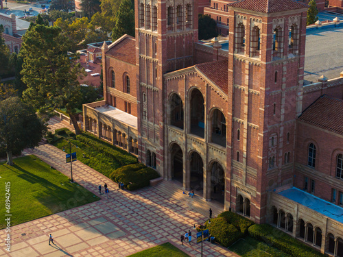 Aerial view of UCLA's Royce Hall, featuring Gothic Revival architecture with twin towers, arched windows, and a red-tiled roof, bathed in golden sunlight on a clear day. photo