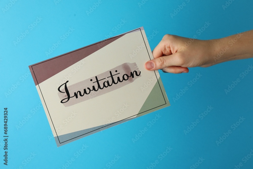 Woman holding beautiful card with word Invitation on light blue background, closeup Woman holding beautiful card with word Invitation on light blue background, closeup