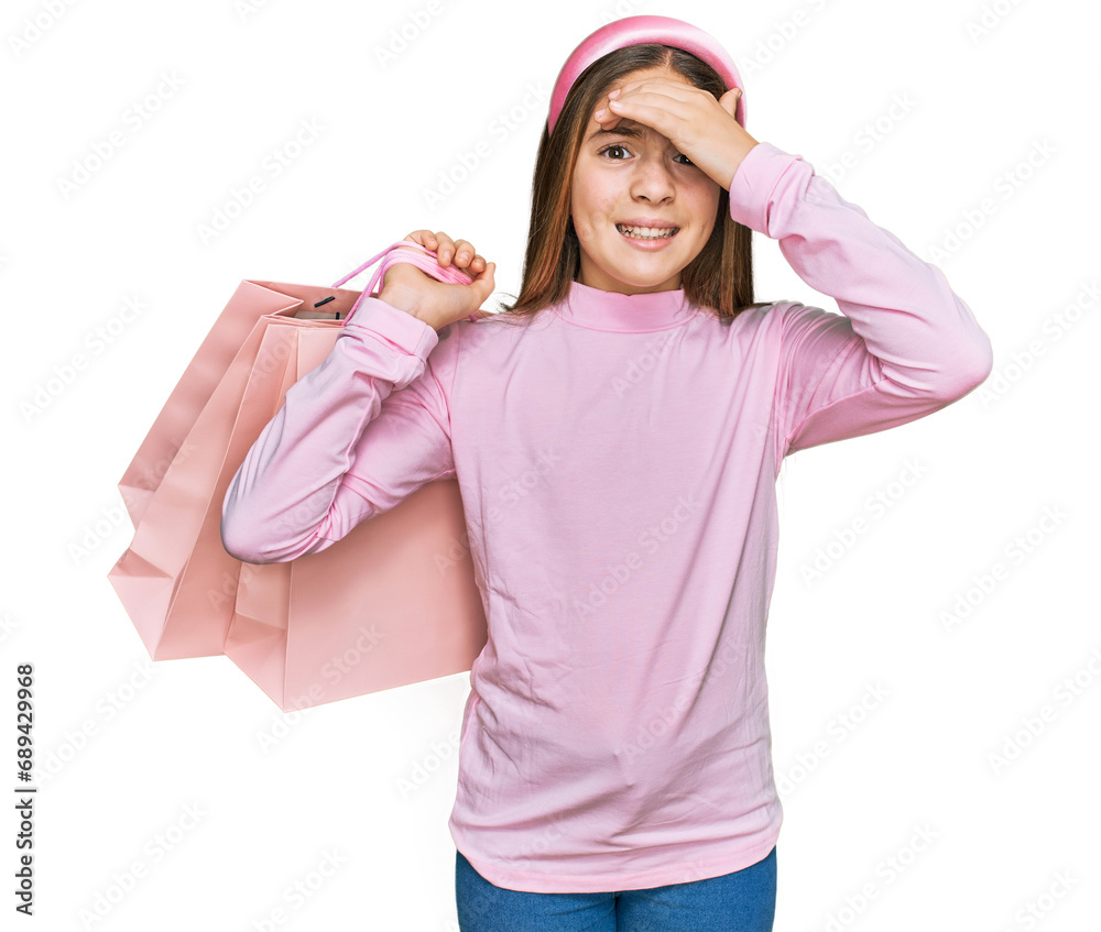 Beautiful brunette little girl holding shopping bags stressed and frustrated with hand on head, surprised and angry face