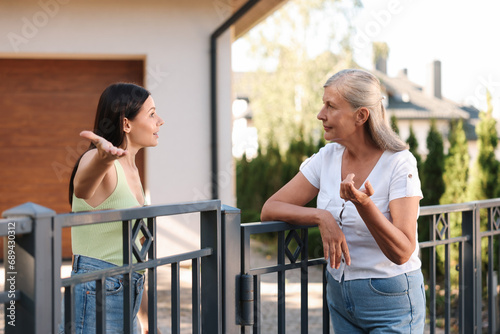 Emotional neighbours having argument near fence outdoors photo