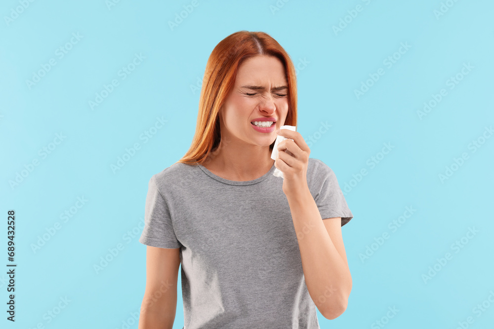 Suffering from allergy. Young woman with tissue sneezing on light blue background Suffering from allergy. Young woman with tissue sneezing on light blue background