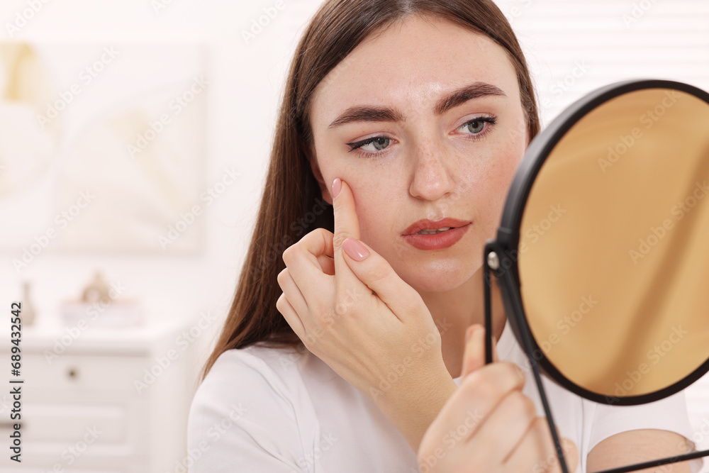 Young woman with skin problem looking at mirror in room Young woman with skin problem looking at mirror in room
