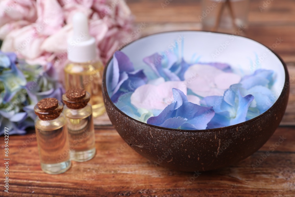 Spa composition. Aromatic water in bowl, bottles of essential oil and flowers on wooden table, closeup Spa composition. Aromatic water in bowl, bottles of essential oil and flowers on wooden table, closeup