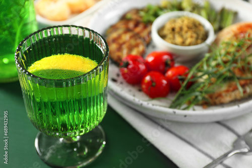 Delicious drink with tarragon in glass on green table, closeup. Space for text photo