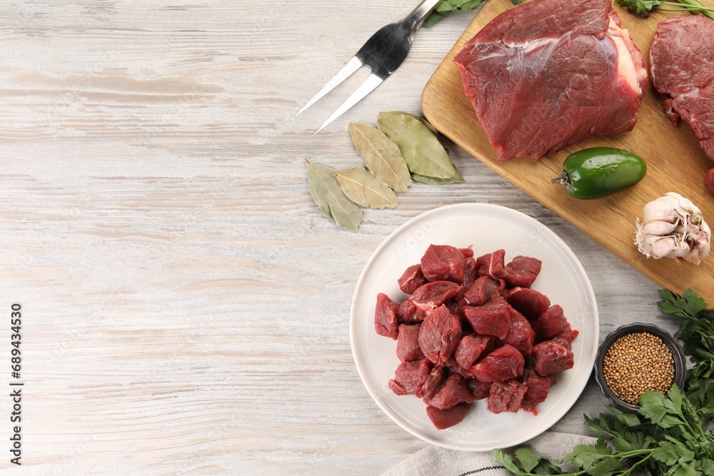 Pieces of raw beef meat, spices and products on light wooden table, flat lay. Space for text