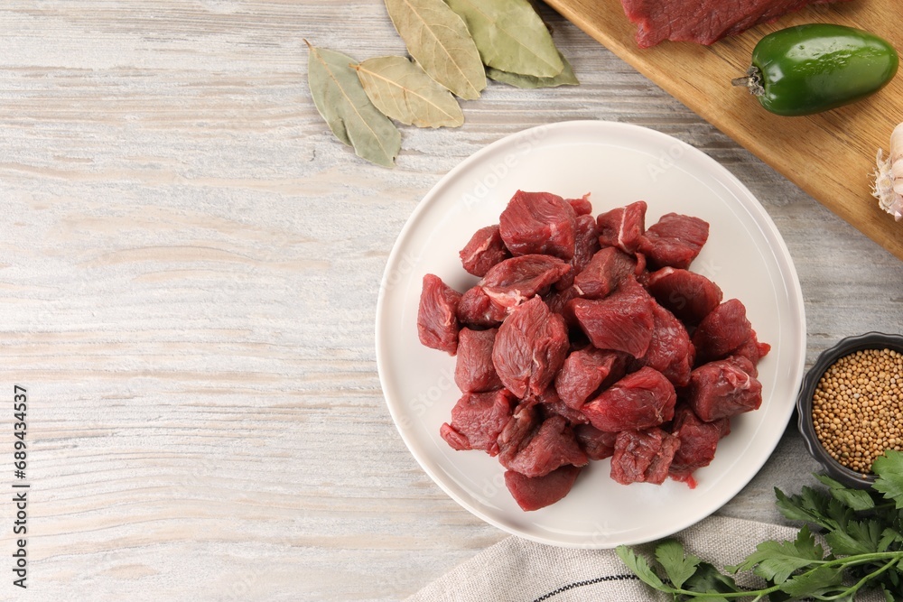 Pieces of raw beef meat, spices and products on light wooden table, flat lay. Space for text Pieces of raw beef meat, spices and products on light wooden table, flat lay. Space for text