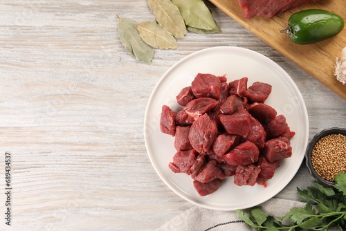 Pieces of raw beef meat, spices and products on light wooden table, flat lay. Space for text