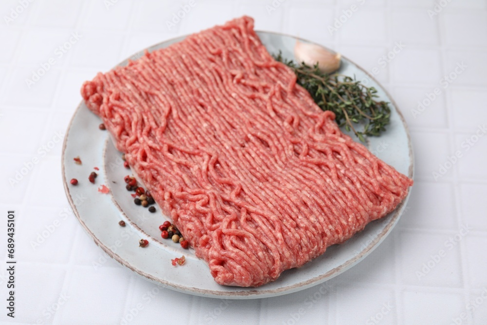 Fresh raw ground meat, peppercorns, garlic and thyme on white tiled table, closeup Fresh raw ground meat, peppercorns, garlic and thyme on white tiled table, closeup