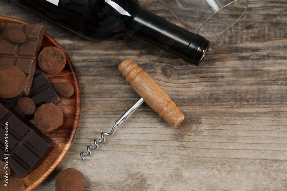 Bottle of red wine, glass, chocolate sweets and corkscrew on wooden table, above view. Space for text