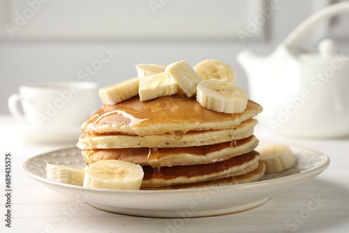 Delicious pancakes with bananas, honey and butter on white wooden table, closeup