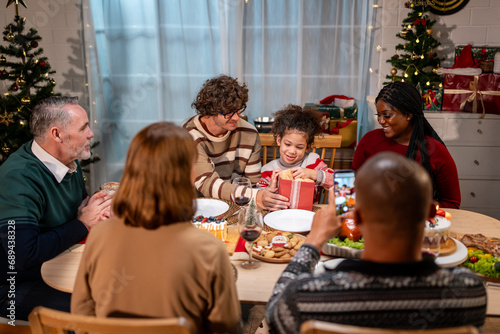 Multi-ethnic family giving gift box to daughter during Christmas party. 