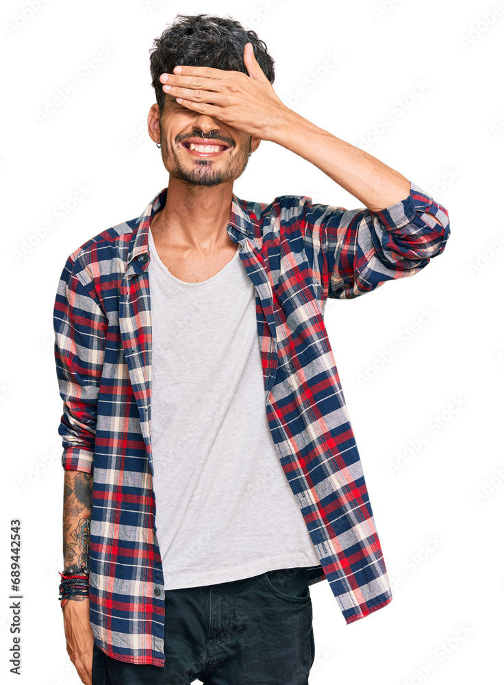 Young hispanic man wearing casual clothes smiling and laughing with hand on face covering eyes for surprise. blind concept. Young hispanic man wearing casual clothes smiling and laughing with hand on face covering eyes for surprise. blind concept.