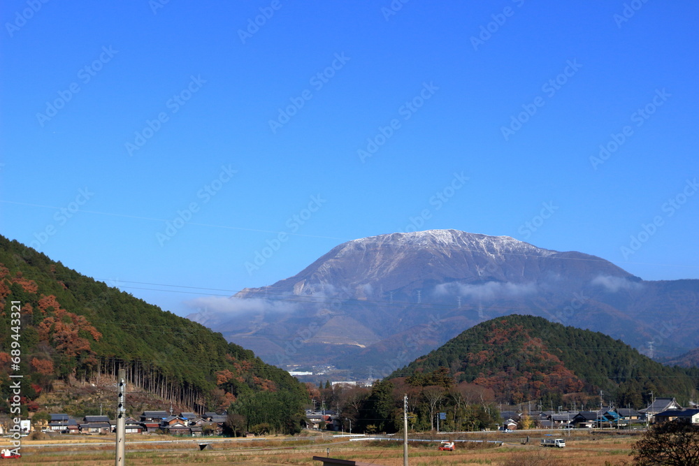 紅葉した山の奥に見える雪が積もった伊吹山と山腹に浮かぶ雲　青空の背景