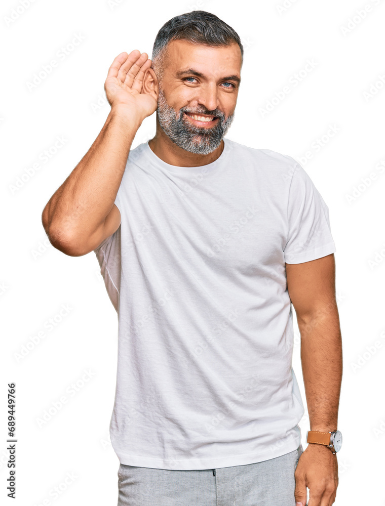Middle age handsome man wearing casual white tshirt smiling with hand over ear listening an hearing to rumor or gossip. deafness concept. Middle age handsome man wearing casual white tshirt smiling with hand over ear listening an hearing to rumor or gossip. deafness concept.