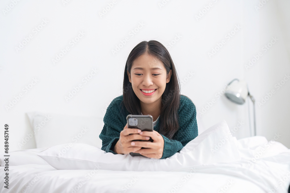 Cute Asian woman lying on bed using phone, exploring social media in the morning. Cute Asian woman lying on bed using phone, exploring social media in the morning.