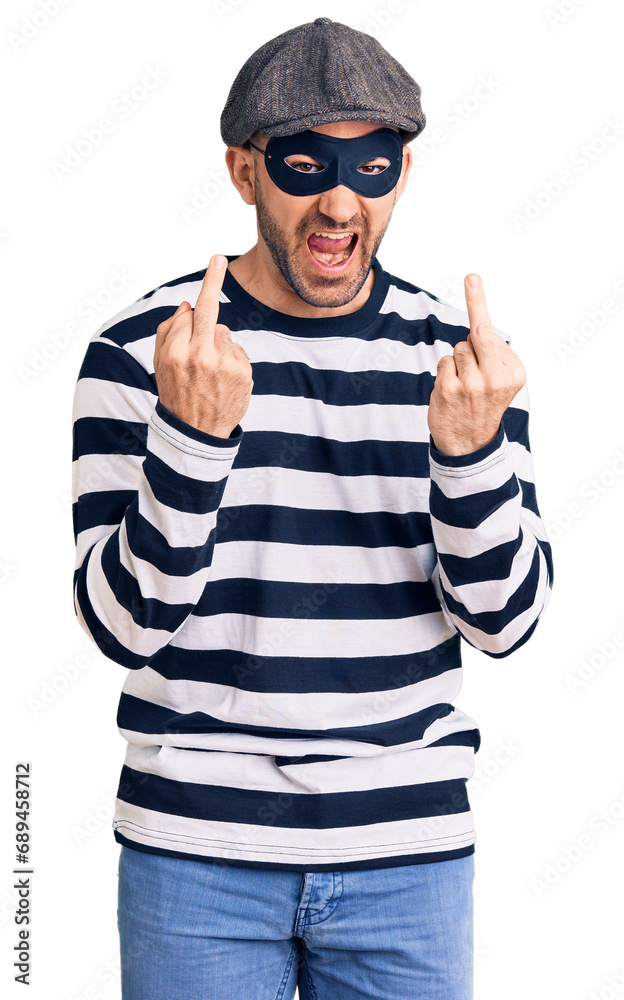 Young handsome man wearing burglar mask showing middle finger doing fuck you bad expression, provocation and rude attitude. screaming excited Young handsome man wearing burglar mask showing middle finger doing fuck you bad expression, provocation and rude attitude. screaming excited