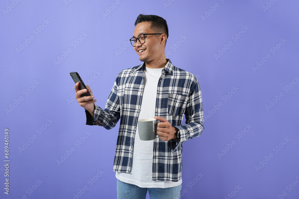 Photo of a young Asian man cheerful bristled guy holding a smartphone screen, wearing a shirt and isolated on a purple background. Photo of a young Asian man cheerful bristled guy holding a smartphone screen, wearing a shirt and isolated on a purple background.