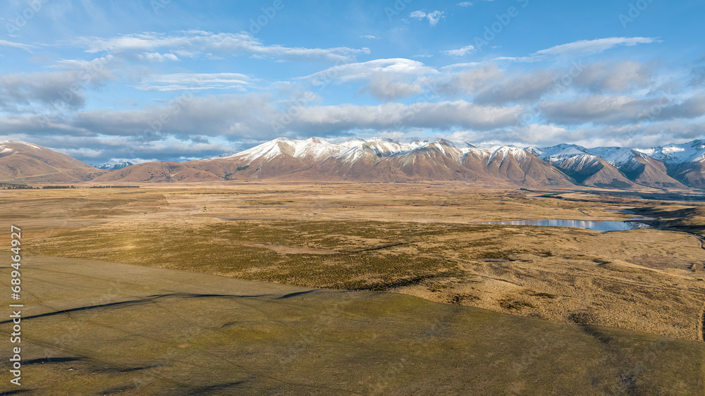 Drone  perspective of the rural and remote country road through arid tundra desert land to the snow capped mountains and Lake